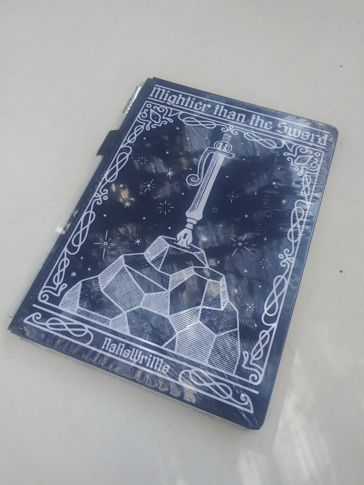 A NanoWrimo notebook. Cover: a pen stuck in a rock point down.